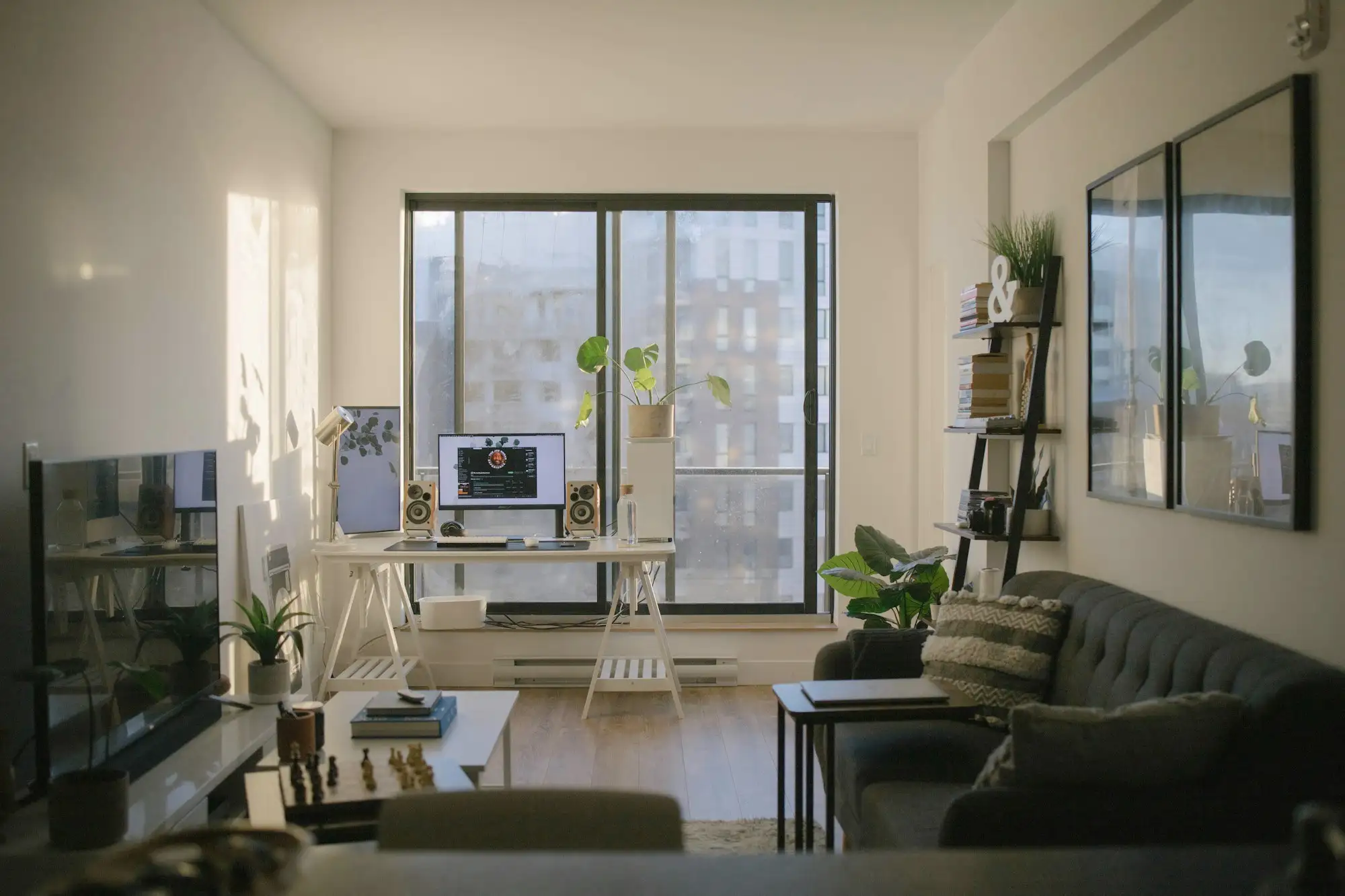 A sunlit living room with a desk, computer and plants beside a large window