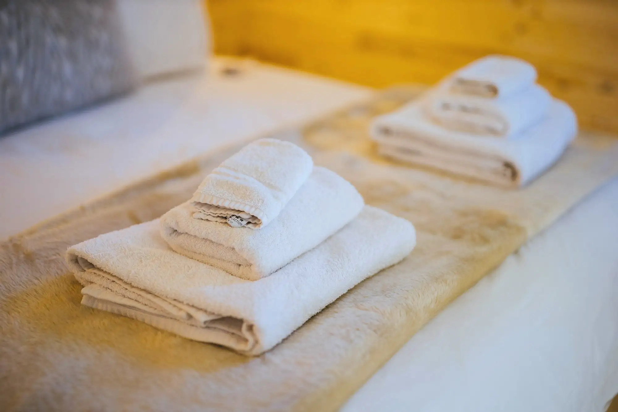 Fresh white towels folded on a neatly made bed in warm light
