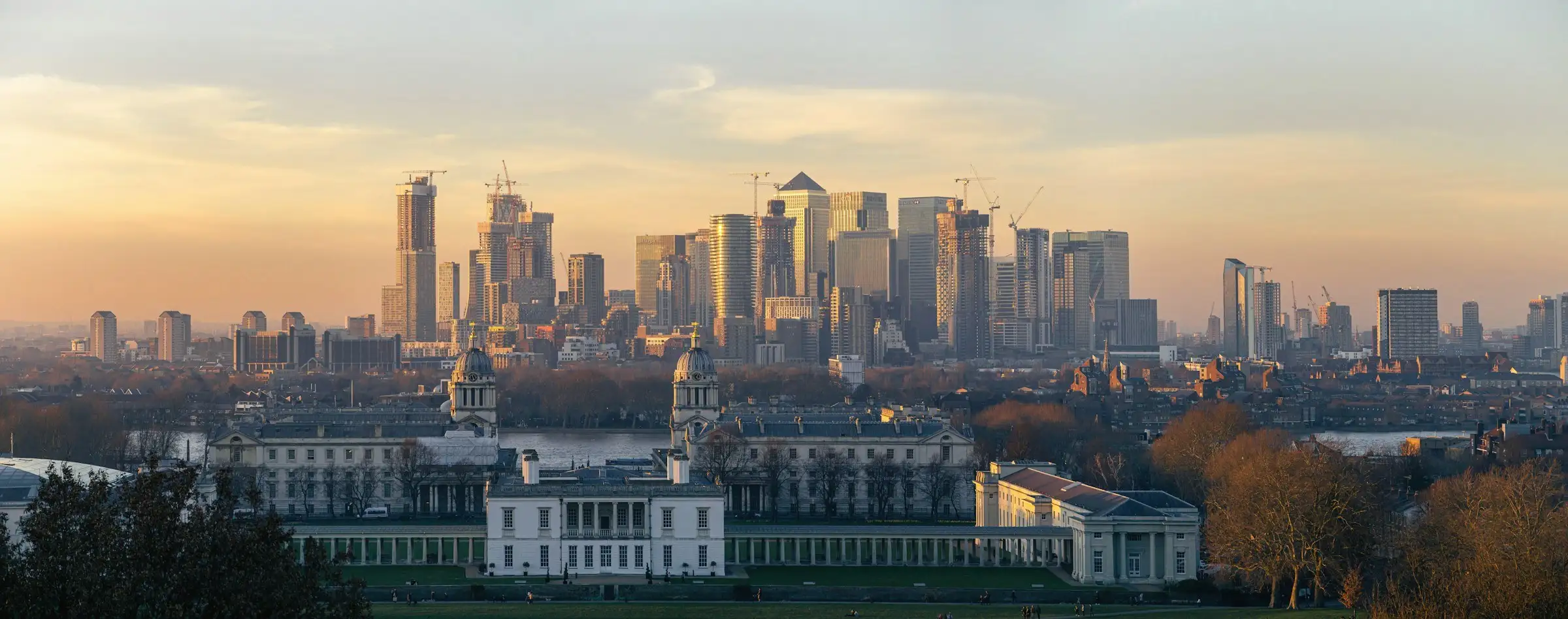 The towers of Canary Wharf at golden hour, seen across the rooftops from Greenwich