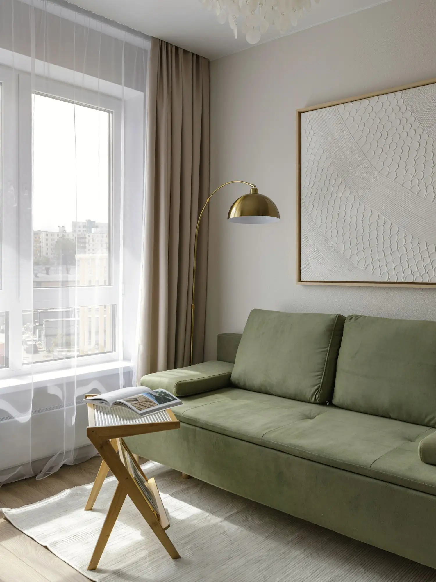 A sage green sofa by a bright window, with a brass floor lamp and textured artwork